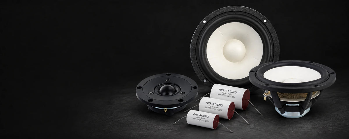 Two white-cone SB Acoustics woofers, a black Satori tweeter and three NB Audio capacitors on a dark background.